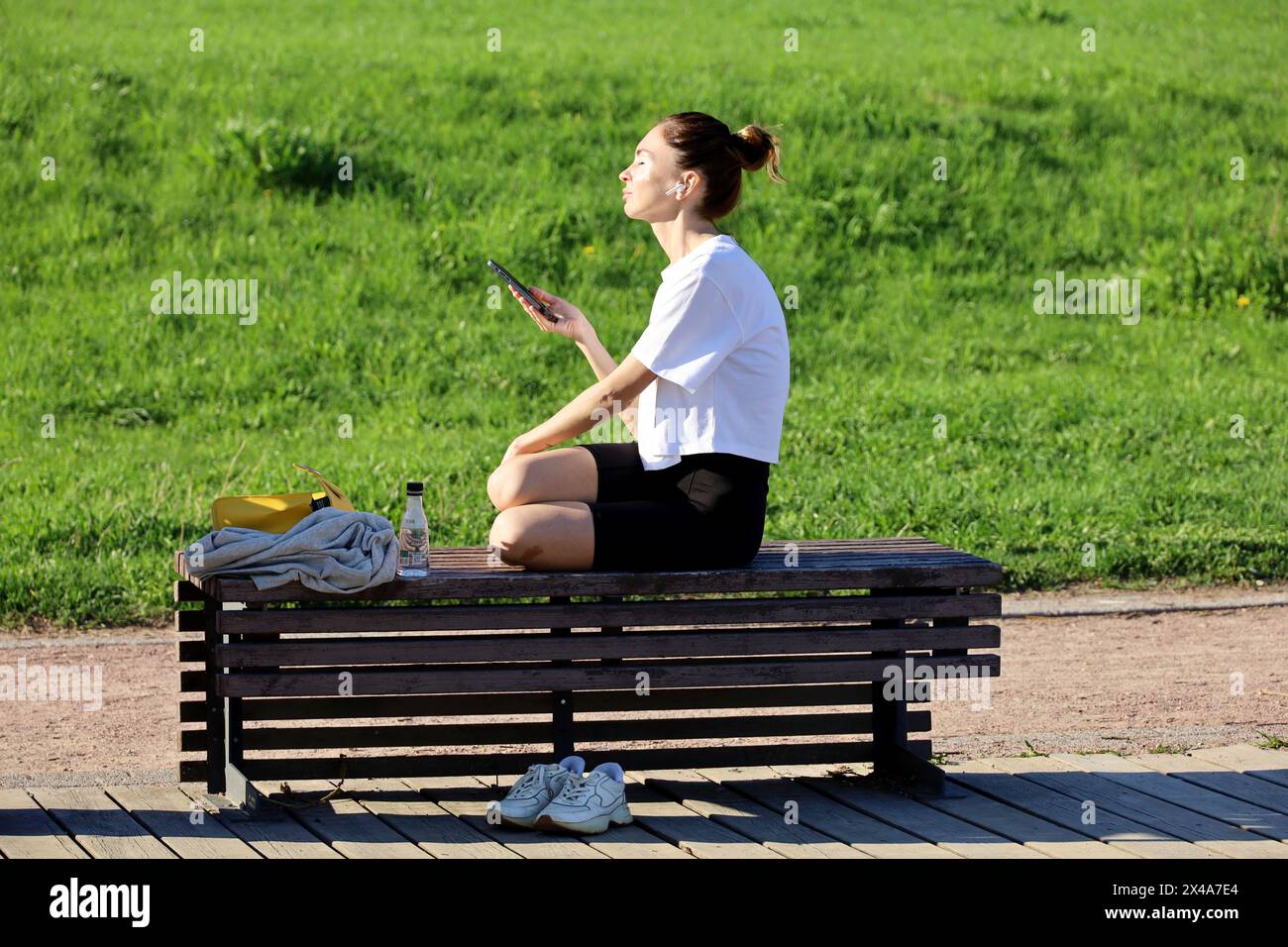 Fille assise sur un banc avec smartphone et casque dans le parc de printemps Banque D'Images