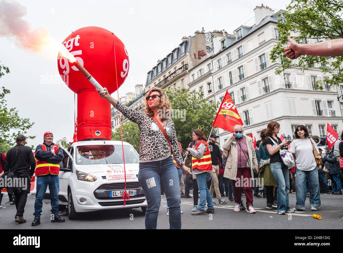 Une femme avec une bombe fumigène rouge devant la voiture de ballon CGT 95 et un bras de quelqu'un donnant un pouce en haut. 1er mai 2024 manifestation à Paris contre l'austérité, pour l'emploi et les salaires. France, Patis le 1er mai 2024. Photographie de Patricia Huchot-Boissier / collectif DyF. Banque D'Images