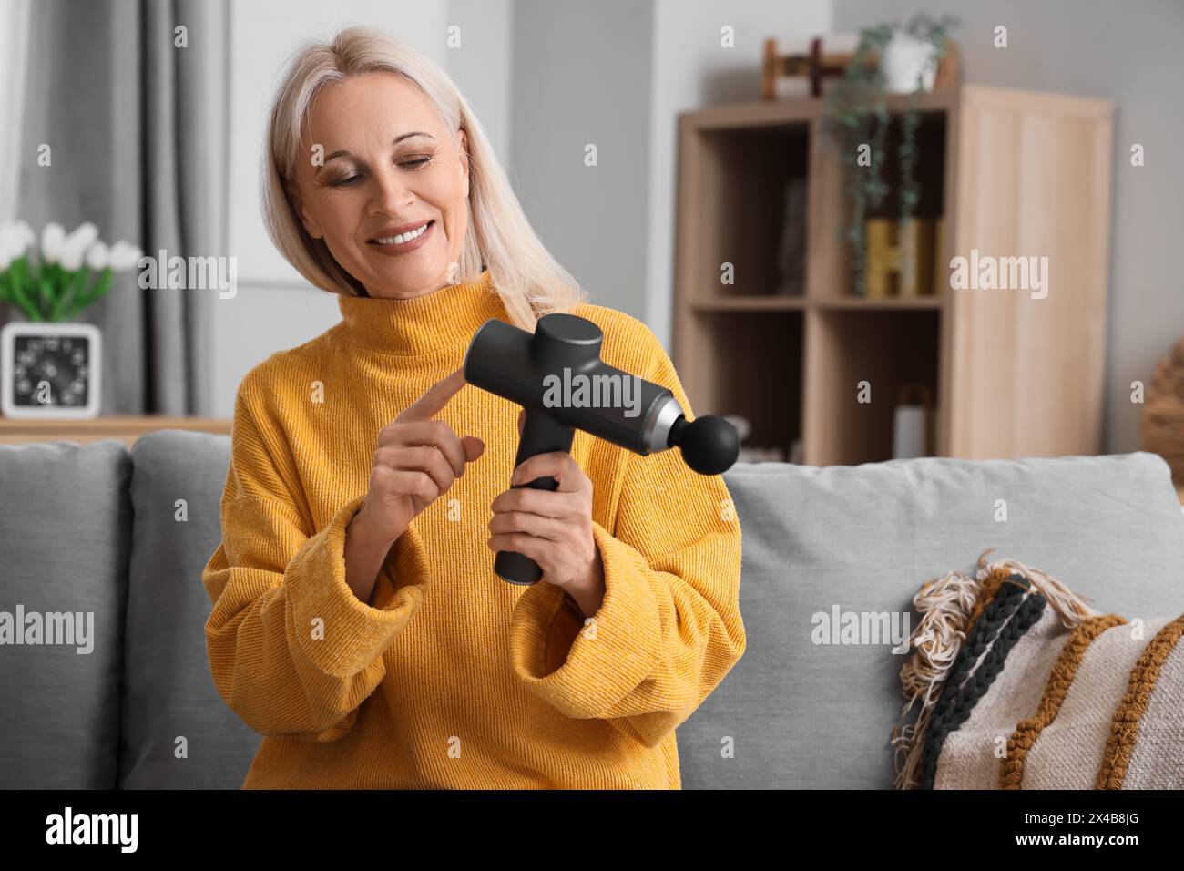 Femme mature avec masseur à percussion à la maison Banque D'Images