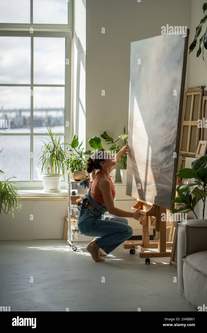 Artiste femme intéressée regardant les détails image d'huile ajuste la toile sur le chevalet pour continuer à peindre. Banque D'Images