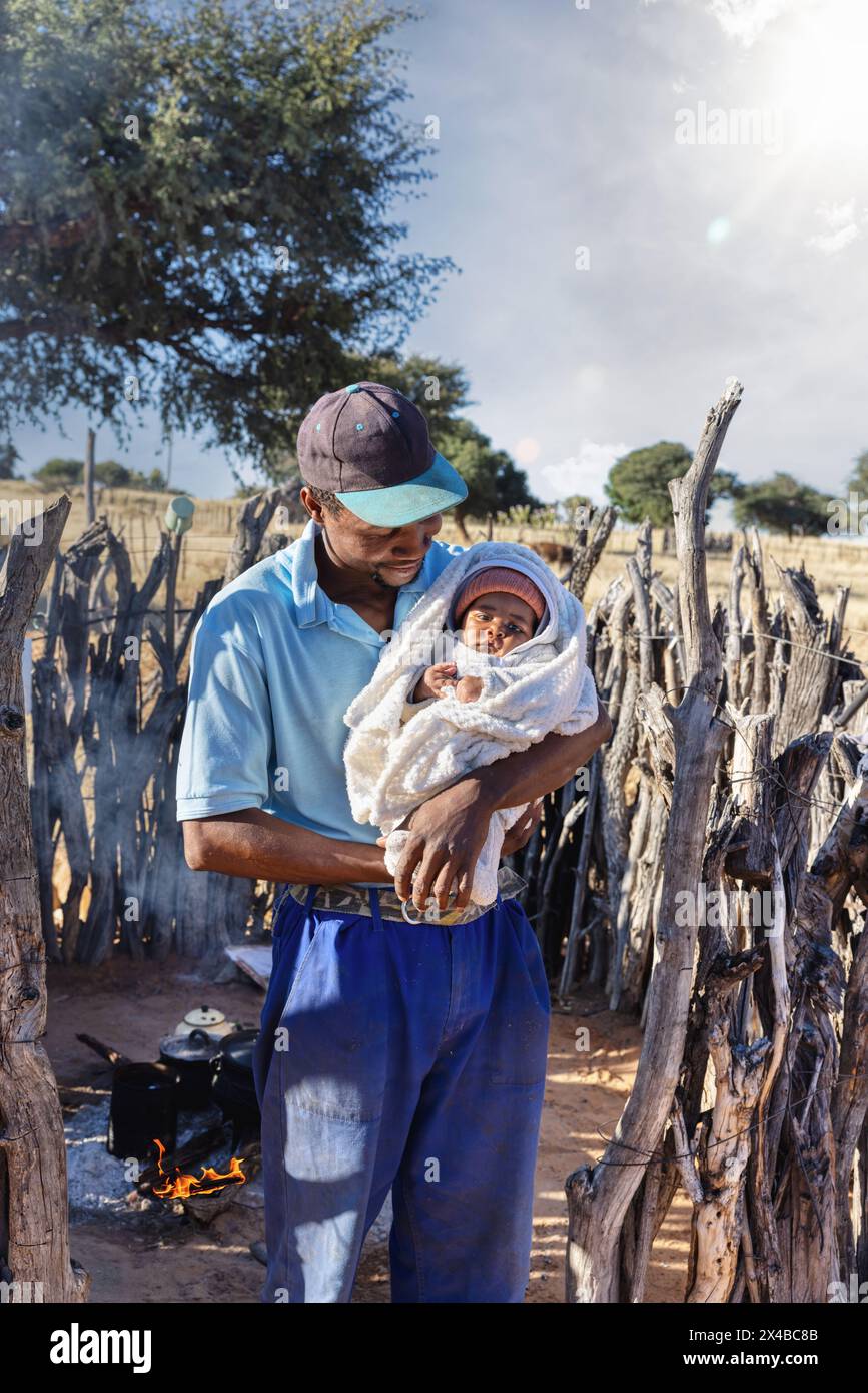 village africain, père africain célibataire tenant le bébé debout devant la cuisine extérieure dans le village, pot sur le feu en arrière-plan Banque D'Images