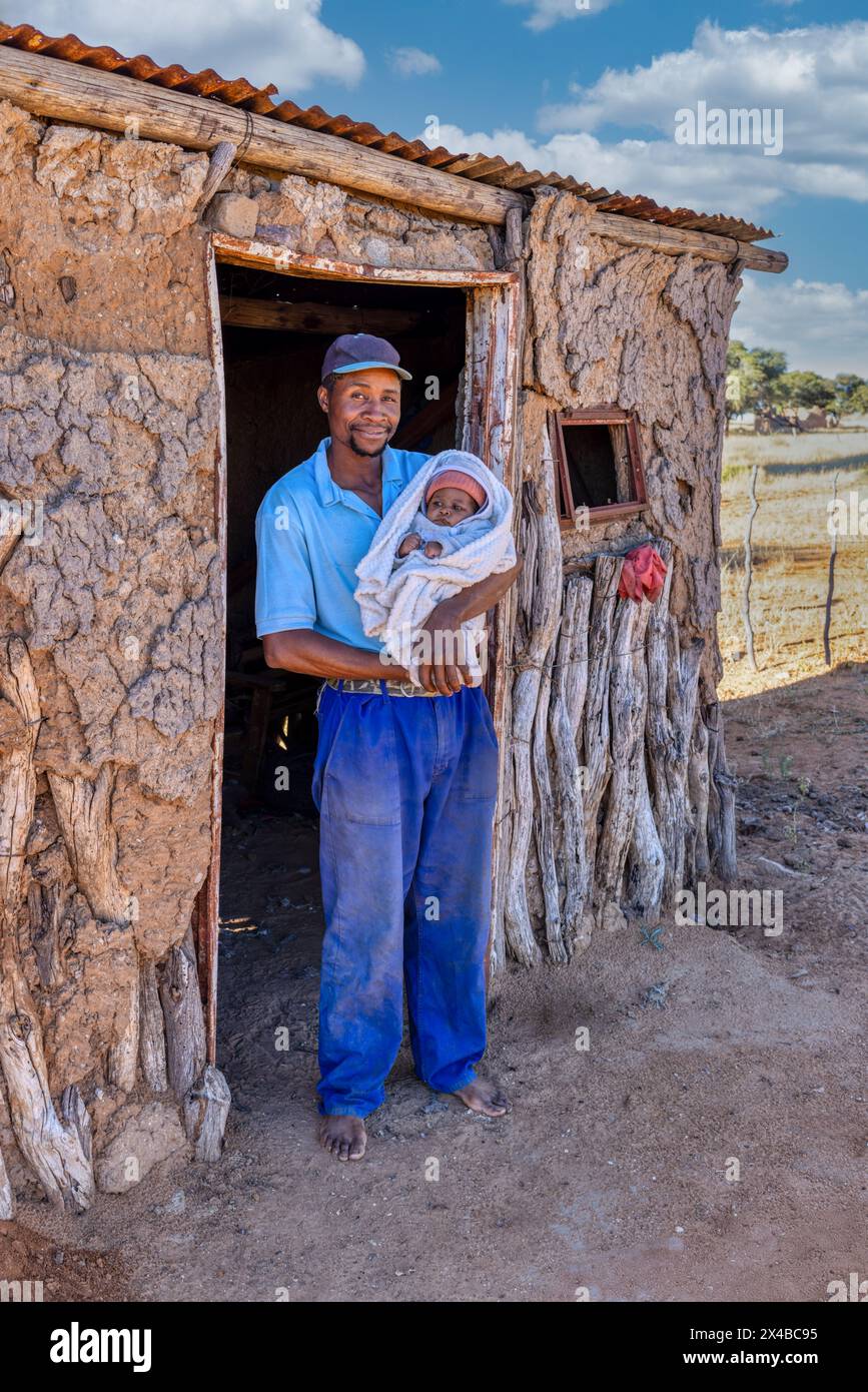 village africain, père africain célibataire tenant le bébé debout devant la maison de boue dans le village Banque D'Images