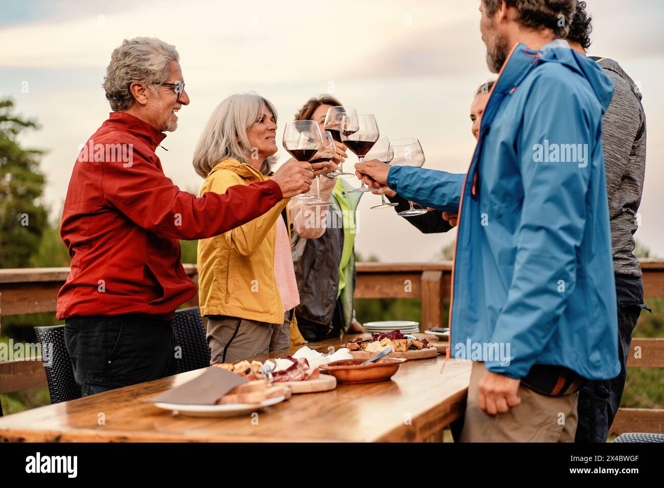 Un groupe d'amis matures - griller avec des verres à vin à une table en plein air, entouré par la nature au coucher du soleil - joyeux rassemblement festif. Banque D'Images