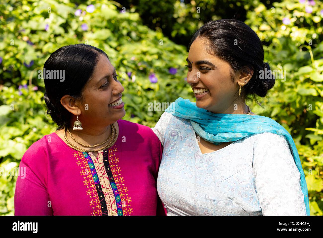 Mère indienne et fille adolescente souriant l'une à l'autre à l'extérieur. Les deux avec les cheveux foncés, jeune femme en haut bleu, femme mature en rose, inaltérée Banque D'Images