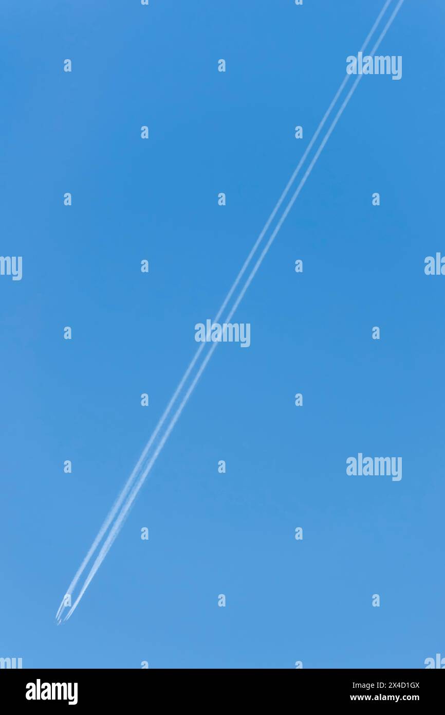 Un avion laisse une longue traînée blanche double contre le ciel bleu Banque D'Images