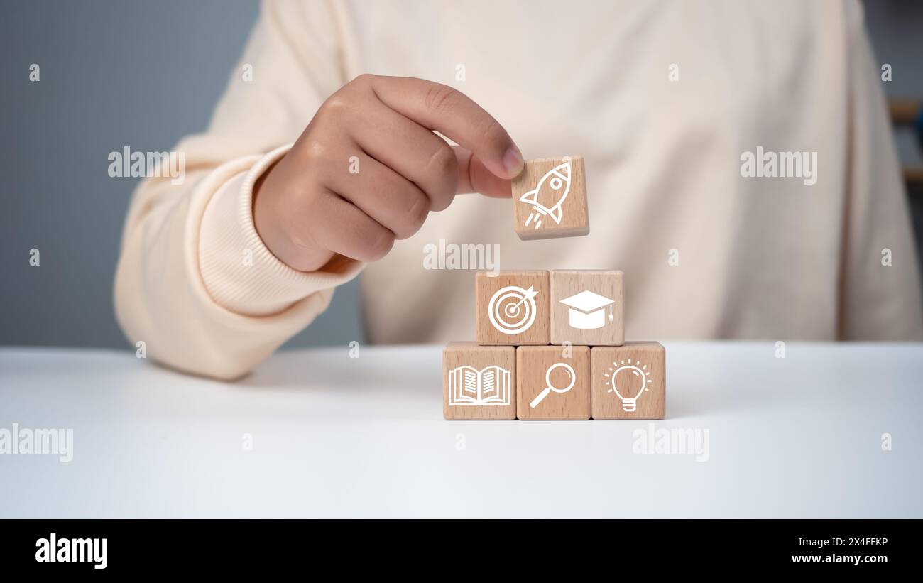 Homme tenant un cube en bois avec des symboles éducatifs imprimés, l'éducation E-learning, des leçons sur Internet et webinaire en ligne. Technologie Internet de l'enseignement. Banque D'Images