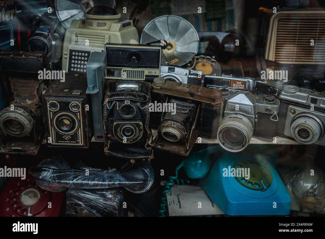 Une collection d'appareils photo vintage, de téléphones et de fans exposés dans une vitrine poussiéreuse d'un magasin d'antiquités. Capture une ambiance nostalgique et le charme du vieux t Banque D'Images