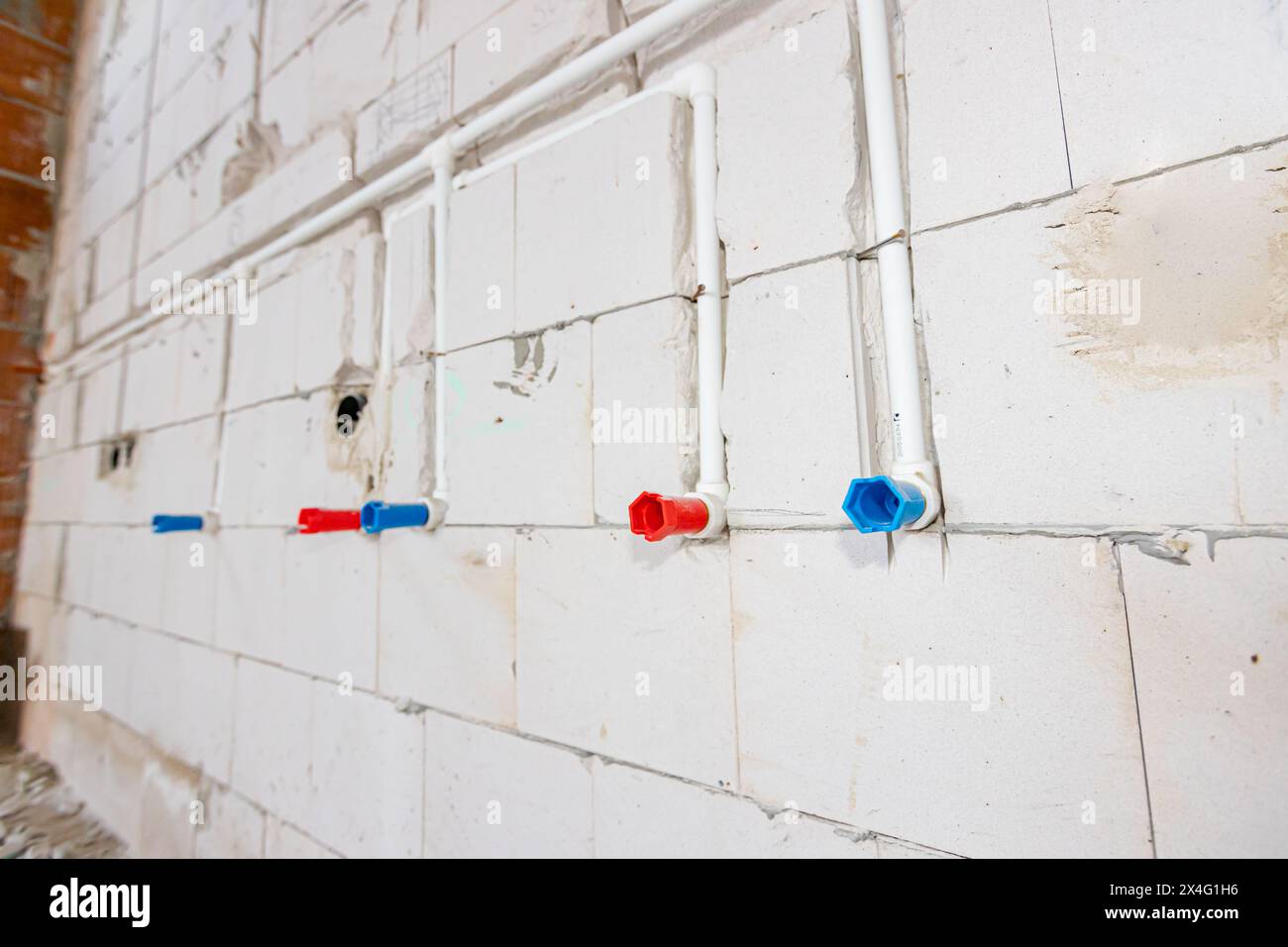 Nouvelle installation de plomberie non finie tuyaux en PVC blanc exposés montés dans le mur. Les tubes rouges et bleus sont pour l'eau chaude et froide. Banque D'Images