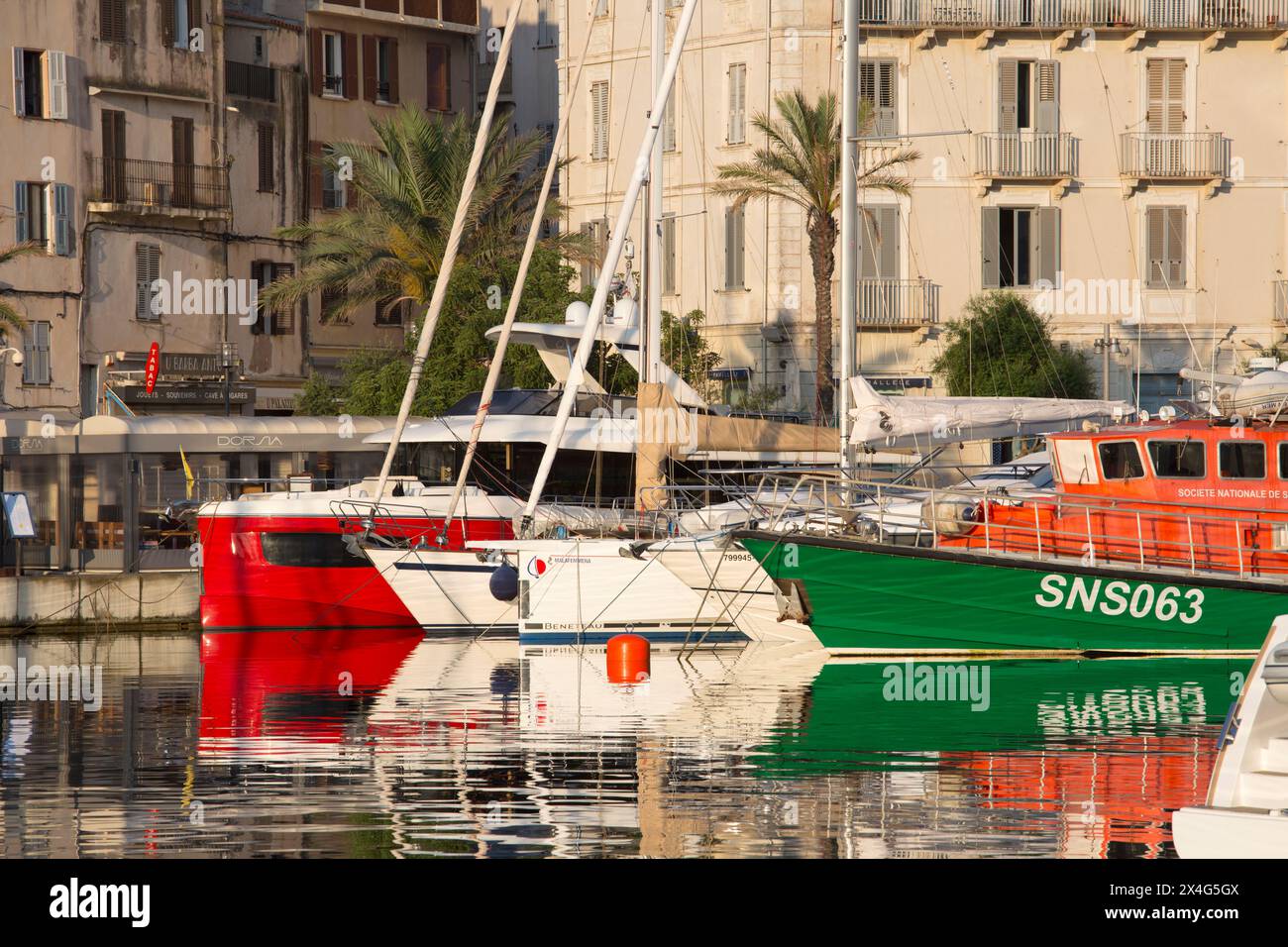 Bonifacio, Corse-du-Sud, Corse, France. Vue sur le port au lever du soleil, bateaux amarrés colorés reflétés dans l'eau tranquille. Banque D'Images