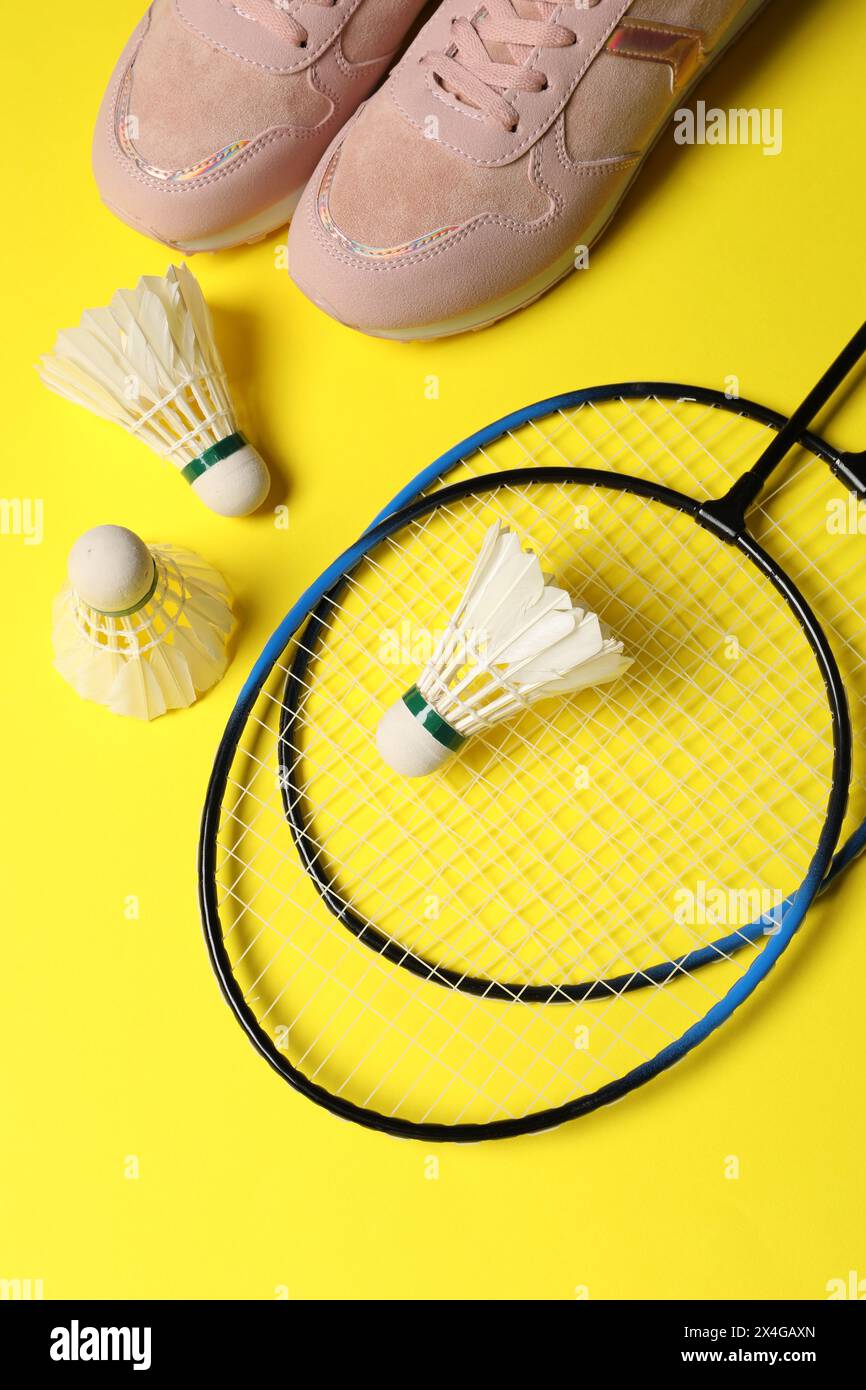 Volants de badminton en plume, raquettes et baskets sur fond jaune, pose à plat Banque D'Images