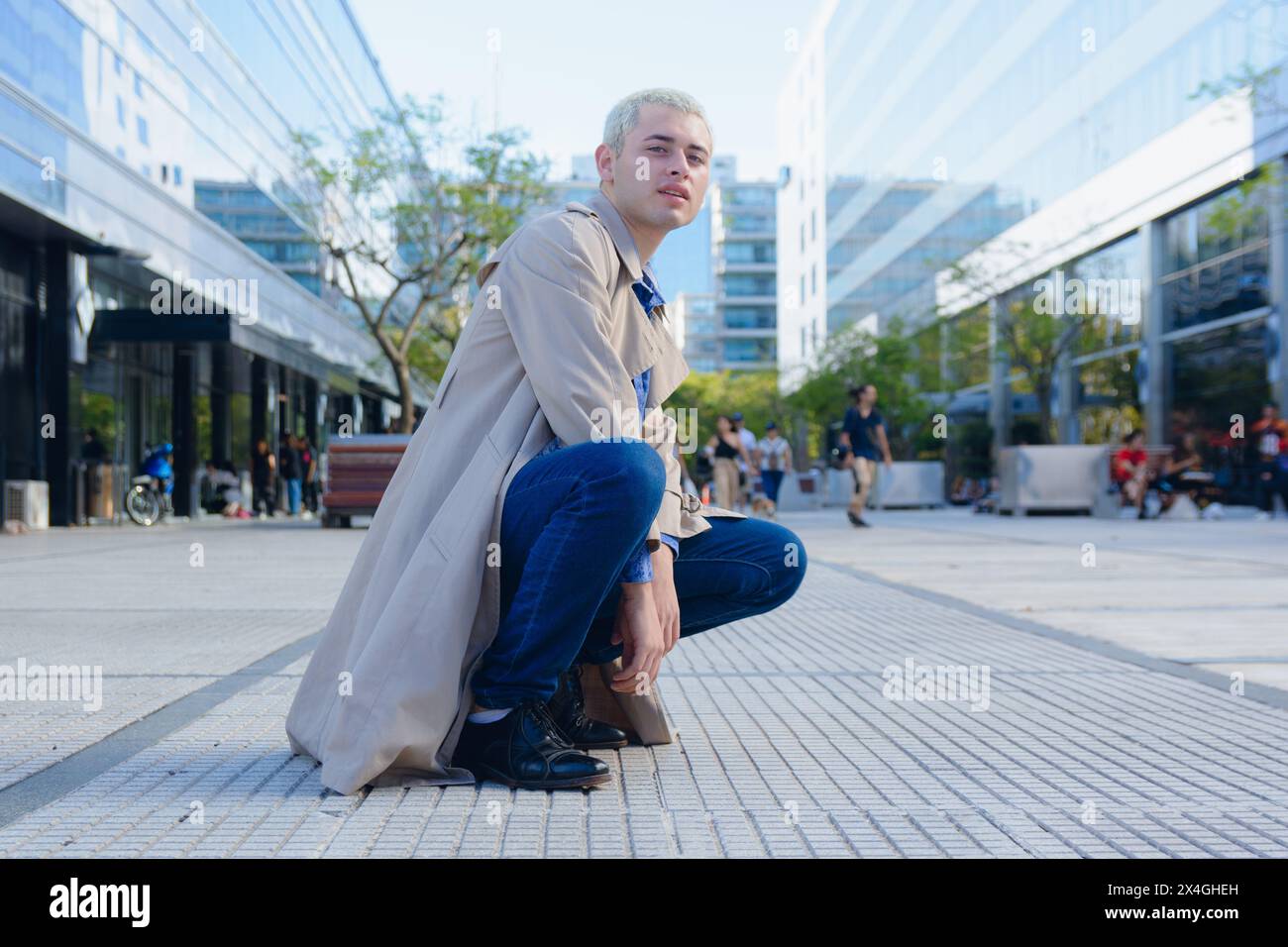 Entrepreneurial jeune homme homosexuel blond cheveux courts latino en dehors des bâtiments de travail commercial accroupis regardant la caméra. Banque D'Images