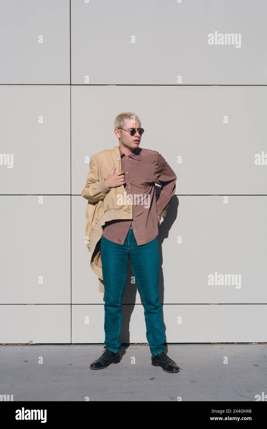 image verticale d'un jeune homme qui est prêt à partir, il est debout enfilant sa veste, il porte des lunettes de soleil. Banque D'Images