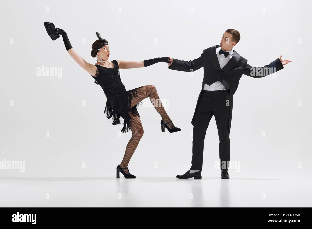 Jeune couple élégant exécutant une danse théâtrale typique de l'âge du jazz, démontrant des gestes ludiques isolés sur fond blanc de studio Banque D'Images