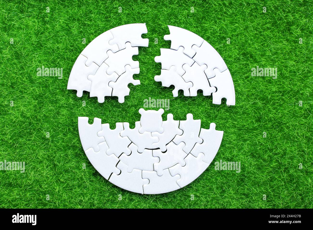 Gros plan d'un puzzle blanc circulaire divisé en trois parties, reposant sur une herbe verte vibrante. Unité, harmonie et concept lié à la nature. Banque D'Images