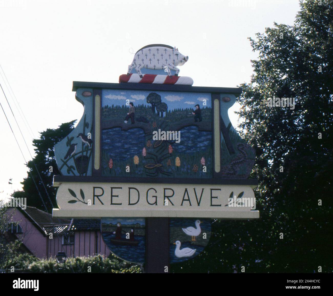 Suffolk. 1987 – photographie du signe du village de Redgrave dans le Suffolk, en Angleterre. Le panneau est fabriqué à la main à partir de bois sculpté et décoré avec des repères et des motifs locaux. Redgrave est situé à environ 4,5 miles à l'ouest de la ville de Diss, et juste au sud de la rivière Waveney qui forme la frontière du comté avec Norfolk. Banque D'Images