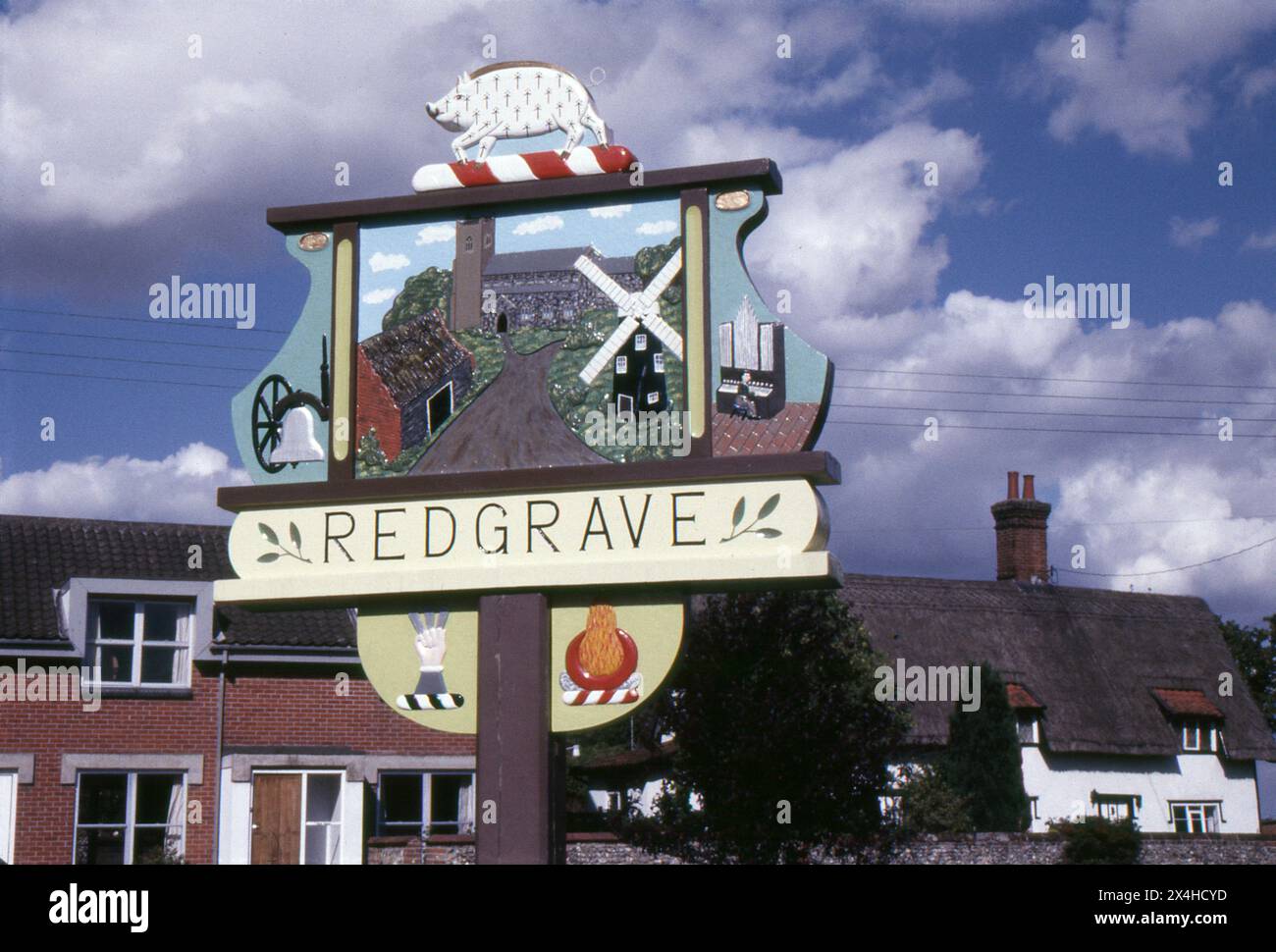 Suffolk. 1987 – photographie du signe du village de Redgrave dans le Suffolk, en Angleterre. Le panneau est fabriqué à la main à partir de bois sculpté et décoré avec des repères et des motifs locaux. Redgrave est situé à environ 4,5 miles à l'ouest de la ville de Diss, et juste au sud de la rivière Waveney qui forme la frontière du comté avec Norfolk. Banque D'Images