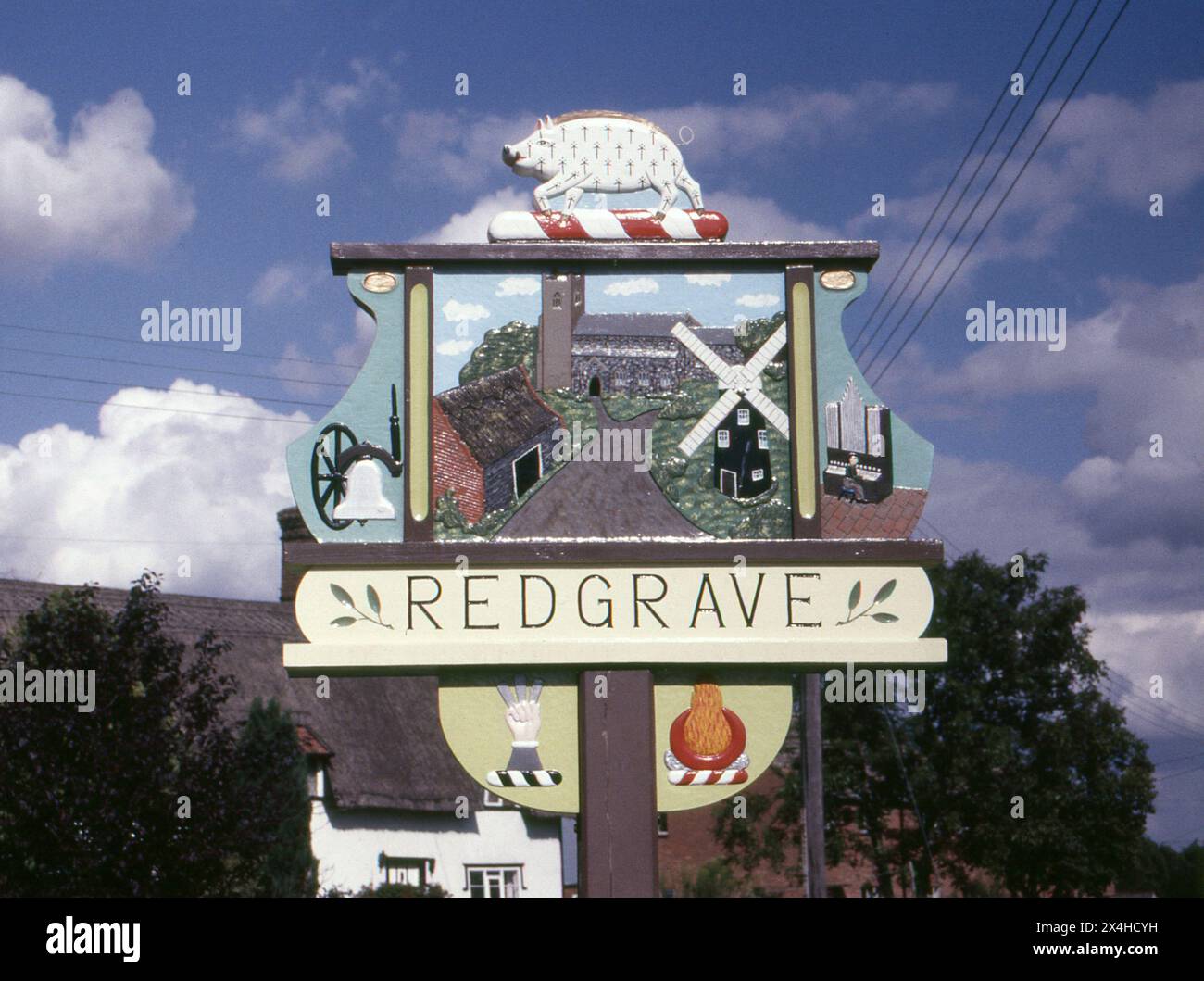 Suffolk. 1987 – photographie du signe du village de Redgrave dans le Suffolk, en Angleterre. Le panneau est fabriqué à la main à partir de bois sculpté et décoré avec des repères et des motifs locaux. Redgrave est situé à environ 4,5 miles à l'ouest de la ville de Diss, et juste au sud de la rivière Waveney qui forme la frontière du comté avec Norfolk. Banque D'Images