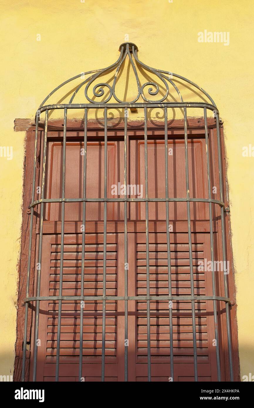 223 le soleil de fin d'après-midi illumine pleinement la grille d'une fenêtre aux volets fermés en bois brun, mur jaune d'une maison coloniale. Trinidad-Cuba. Banque D'Images