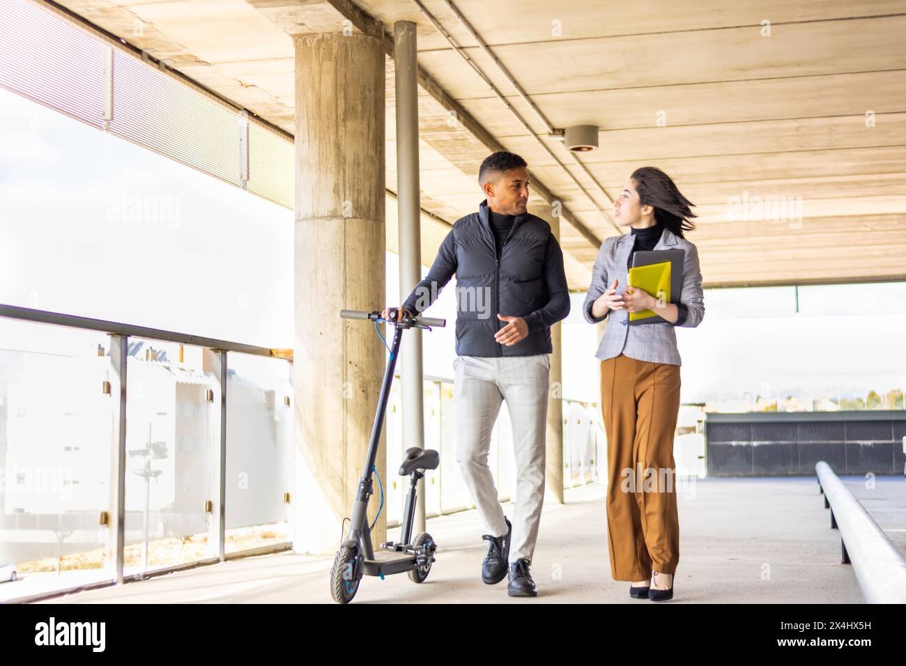 Femme en costume formel parlant à l'homme tenant un scooter. Fille en costume formel parlant à l'homme tenant scooter électrique pendant qu'ils marchent Banque D'Images