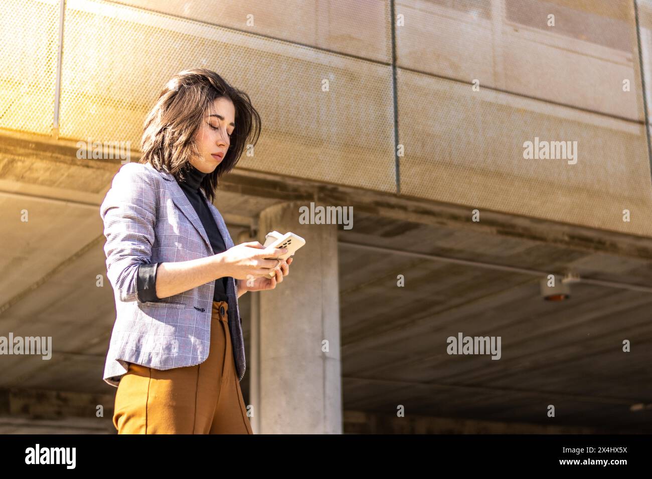 Jeune femme d'affaires marchant dans la rue tenant un téléphone portable et un verre de café, Une femme marchant dans la rue tenant un café en verre et utilisant Banque D'Images