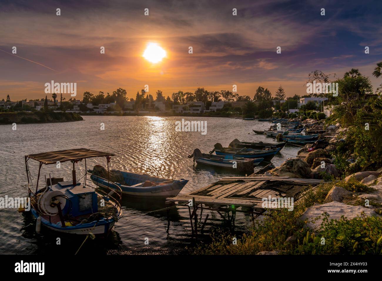 Le magnifique coucher de soleil pittoresque dans la baie de Carthage dans le front de mer tunisien à Tunis avec de petits bateaux de pêche dans l'eau et des nuages roses. Banque D'Images