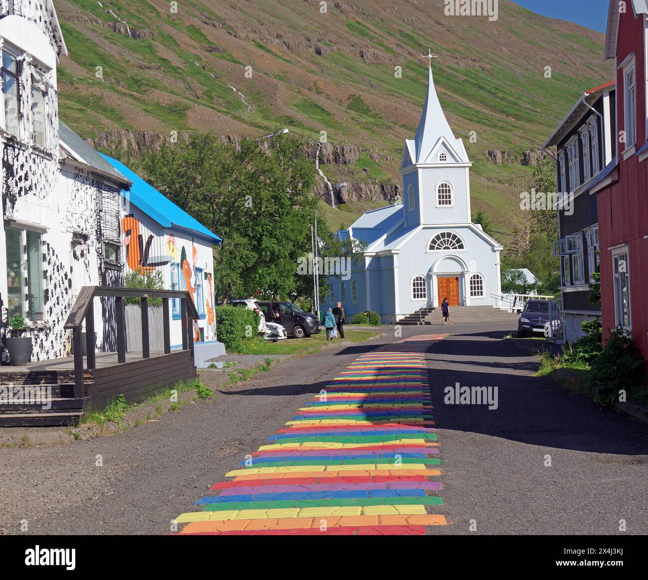 Petite église et maisons bordent une rue décorée de couleurs arc-en-ciel, Seydisfjördur. Islande Banque D'Images
