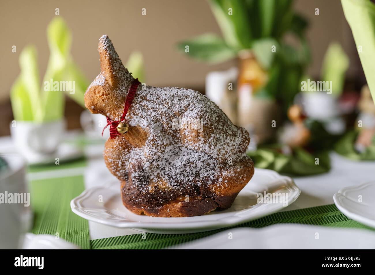 Gâteau de Pâques enrobé de sucre en poudre en forme de lapin avec un ruban rouge sur une table printanière. Banque D'Images