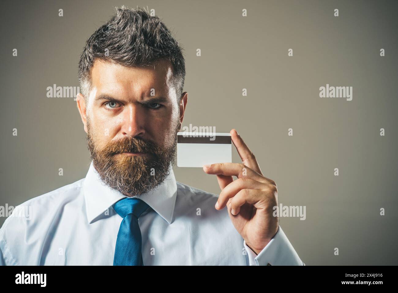 Bel homme barbu en chemise blanche et cravate bleue montrant une carte de crédit avec bande magnétique. Espace de copie pour la publicité des services bancaires, prêt ou Banque D'Images