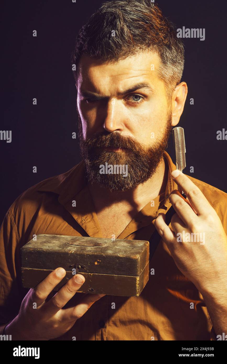 Beau coiffeur barbu dans une chemise élégante avec rasoir droit et boîte en bois dans les mains. Portrait d'homme non rasé prêt à se raser la barbe avec Banque D'Images