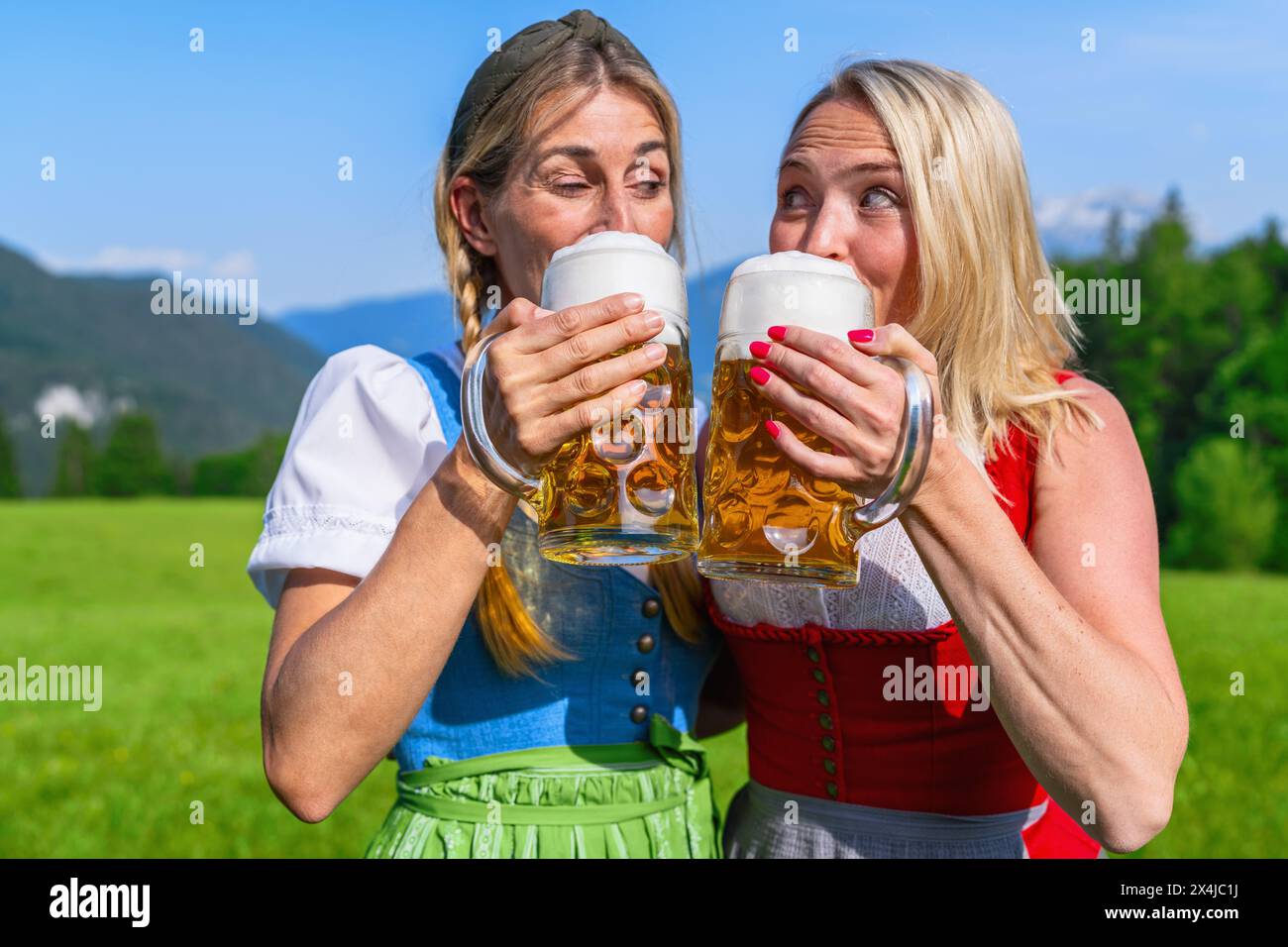 Deux femmes dans le Tracht traditionnel, Dirndl buvant de la bière mousseuse dans des tasses avec des montagnes alpines en arrière-plan, concept Oktoberfest Banque D'Images