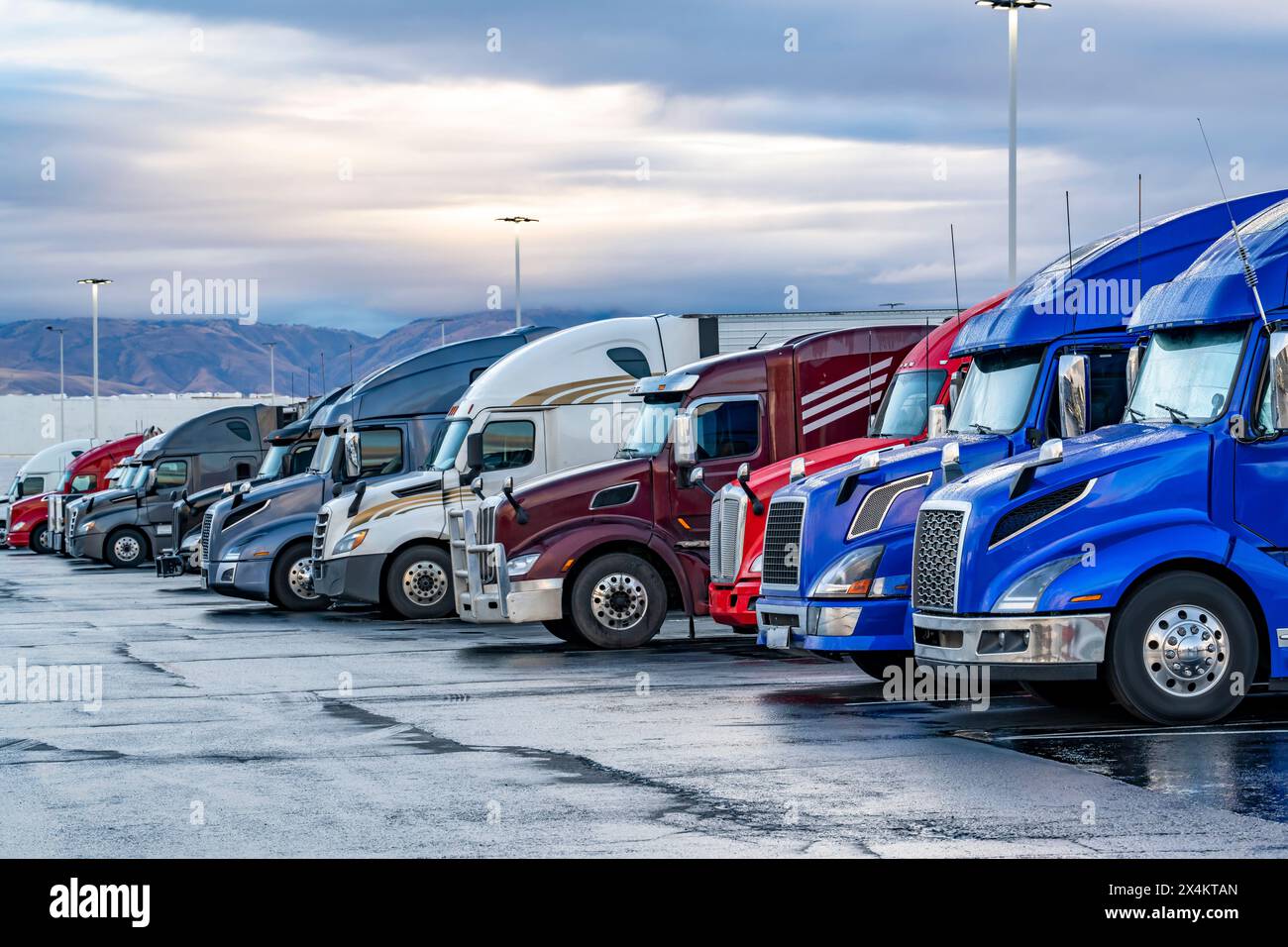 Transporteurs industriels différents tracteurs de semi-remorques de grande taille avec semi-remorques chargées debout en rangée sur le parking d'arrêt de camion à l'heure du matin tak Banque D'Images