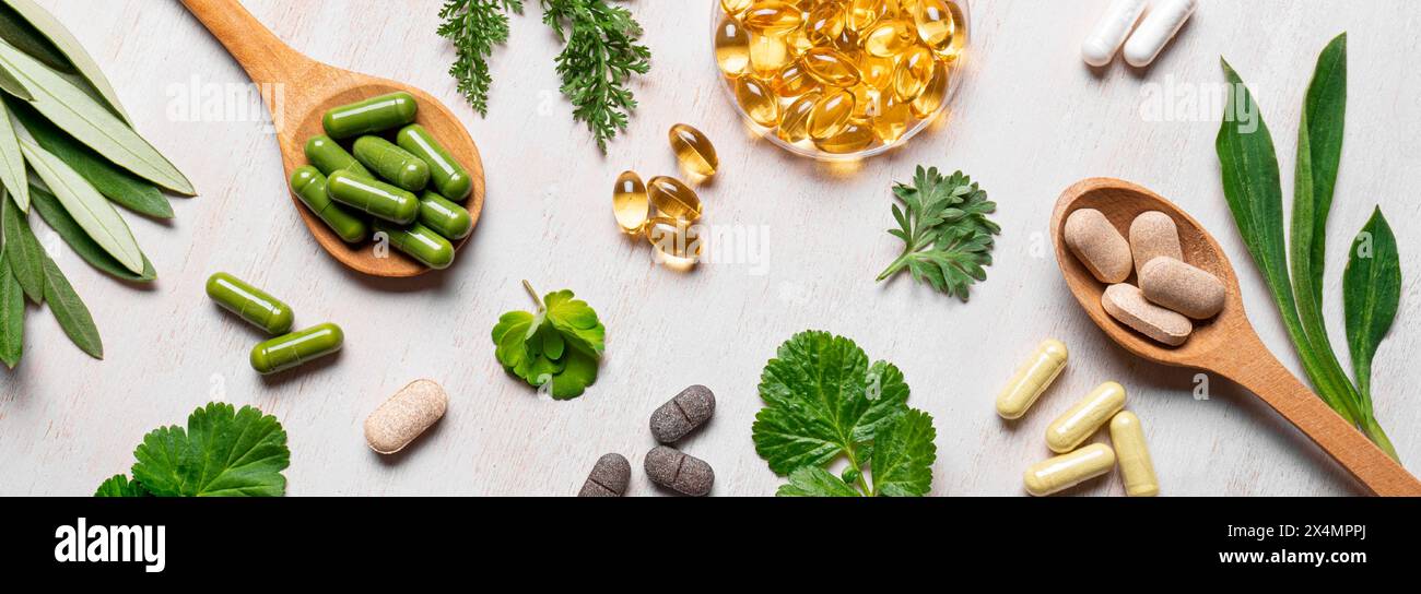 Vitamines naturelles, suppléments à base de plantes et feuilles vertes plates reposent sur fond de bois blanc. Diverses capsules et pilules biologiques, bannière. Banque D'Images