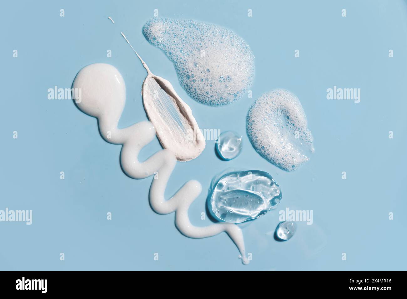Divers produits cosmétiques de soins de la peau frottent la texture des échantillons sur fond bleu. Échantillons de produits démaquillants - gel lavant, mousse moussante et lait. Banque D'Images