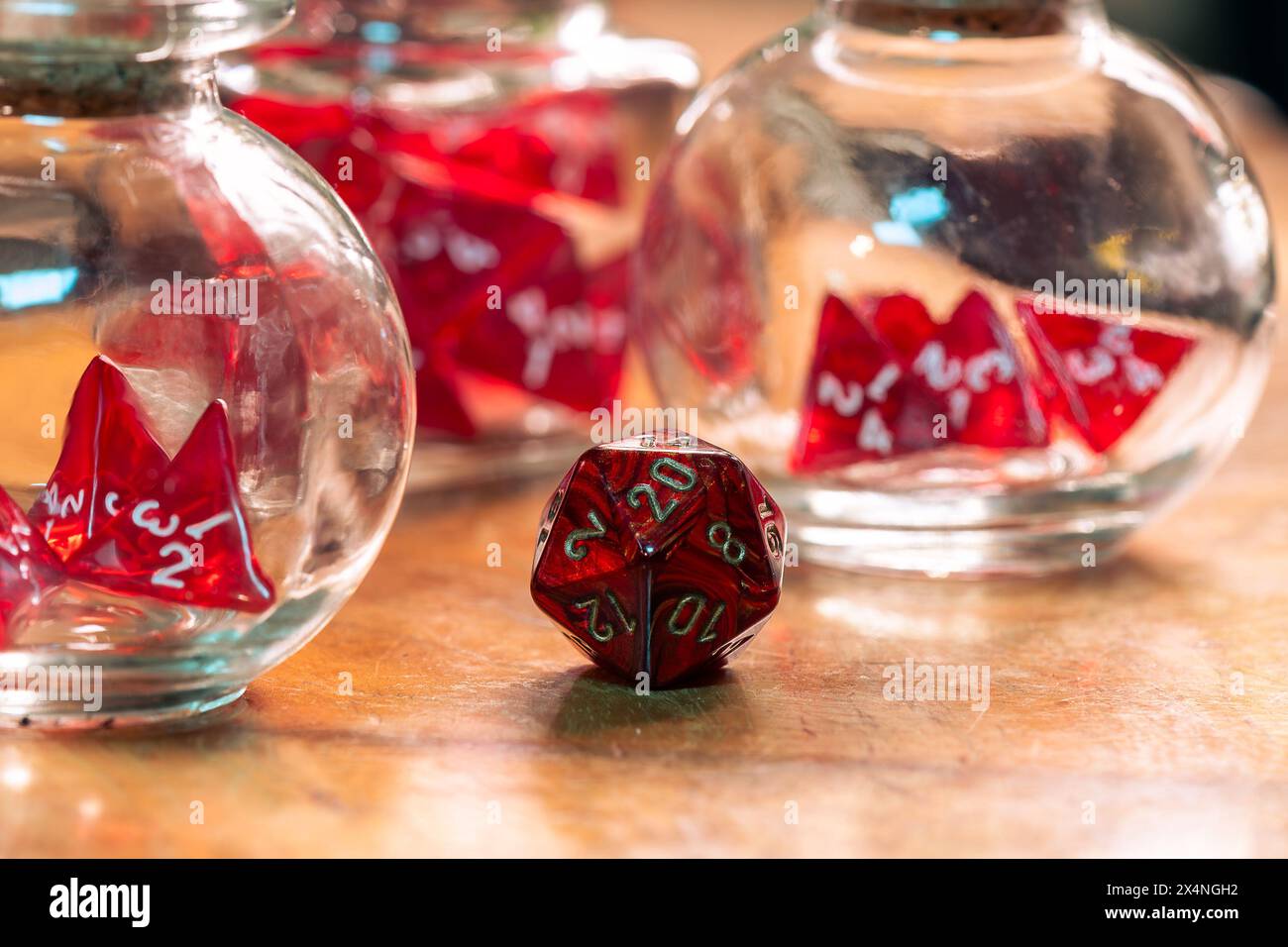 Un seul dé rouge se tient bien en évidence dans la mise au point, contrastant avec des dés flous dans des bocaux en verre en arrière-plan, sur une table en bois rustique Banque D'Images
