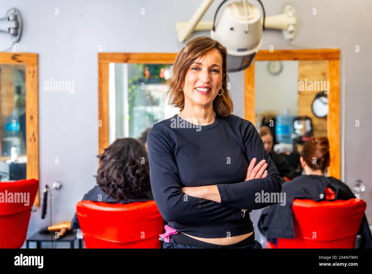 Portrait d'un coiffeur heureux et fier debout avec les bras croisés et souriant à la caméra dans le salon Banque D'Images
