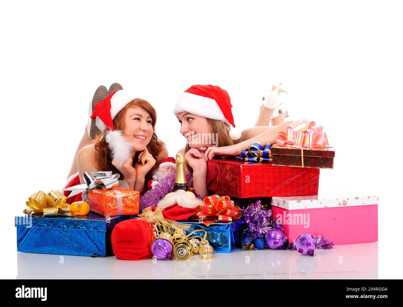 deux jolies femmes en vêtements de noël gisent sur le sol blanc avec des cadeaux, isolées sur blanc Banque D'Images