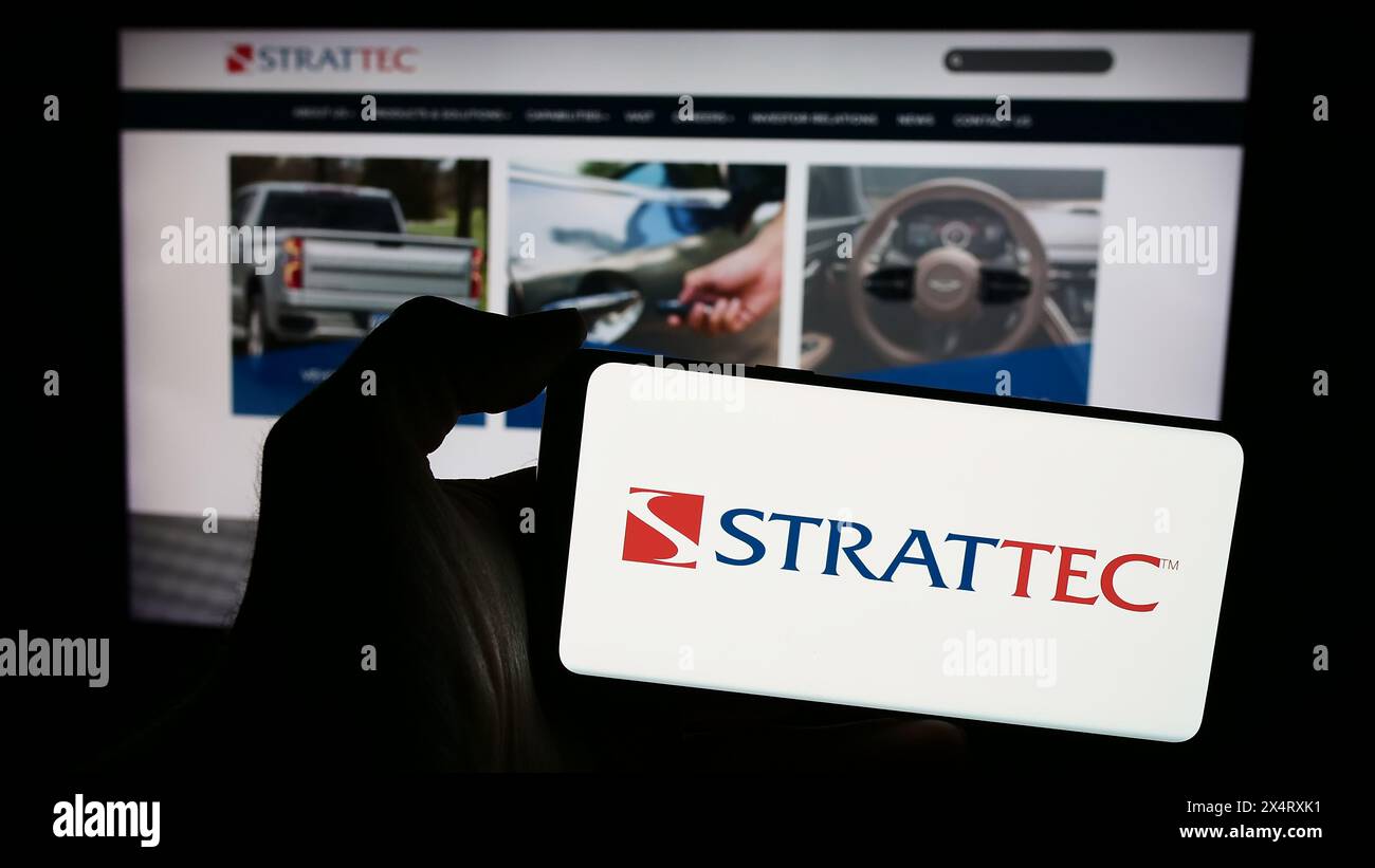 Personne tenant le téléphone portable avec le logo de la société automobile américaine Strattec Security Corporation en face de la page Web. Concentrez-vous sur l'affichage du téléphone. Banque D'Images