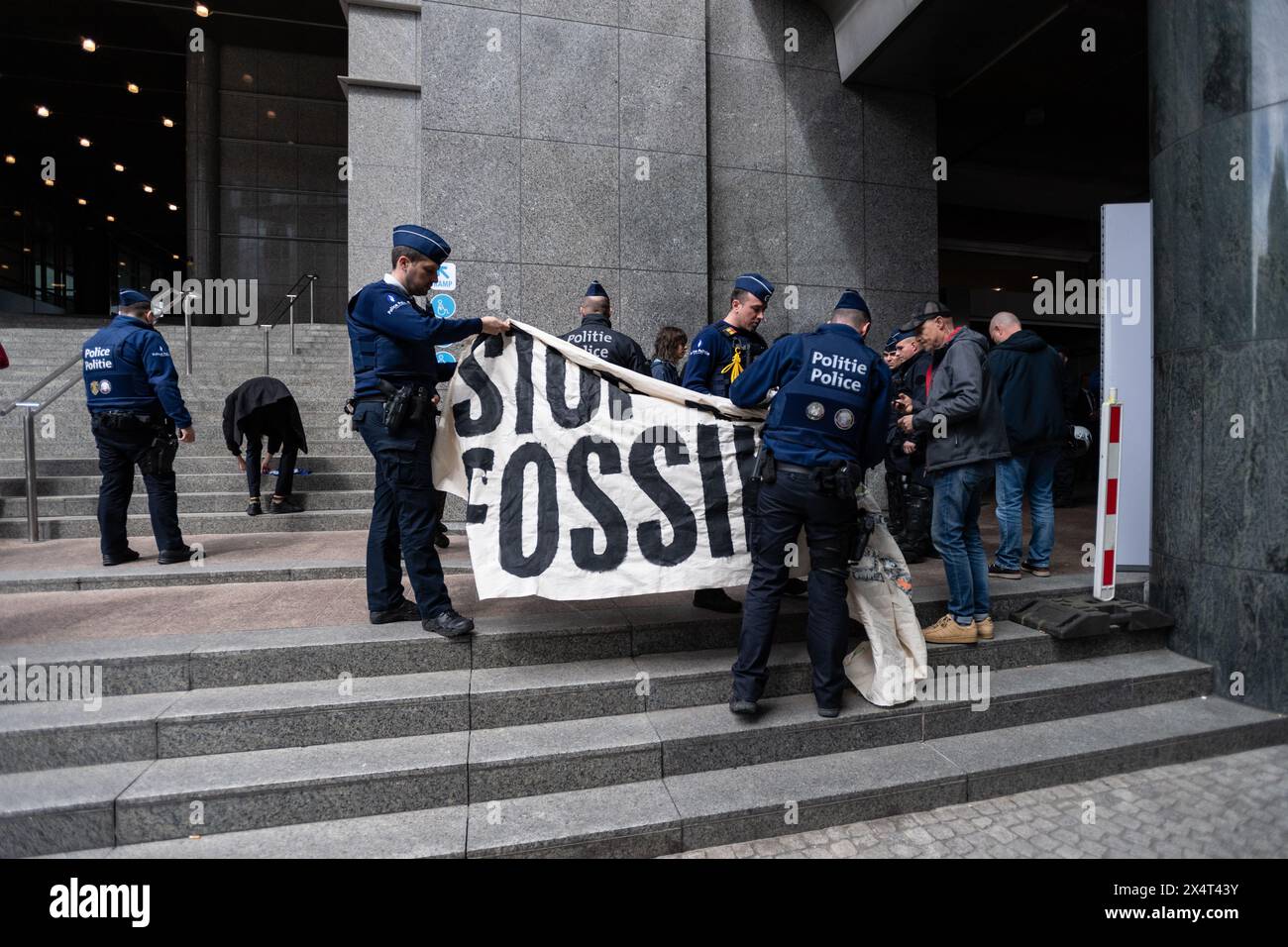 4 mai 2024, Bruxelles, Belgique. La police inspecte une banderole indiquant "arrêtez de financer les combustibles fossiles" tout en détenant plusieurs jeunes manifestants devant le Parlement européen lors de sa journée portes ouvertes au public. Les manifestants ont ensuite été menottés et emmenés dans une camionnette blanche banalisée. Crédit : Alamy Live News Banque D'Images