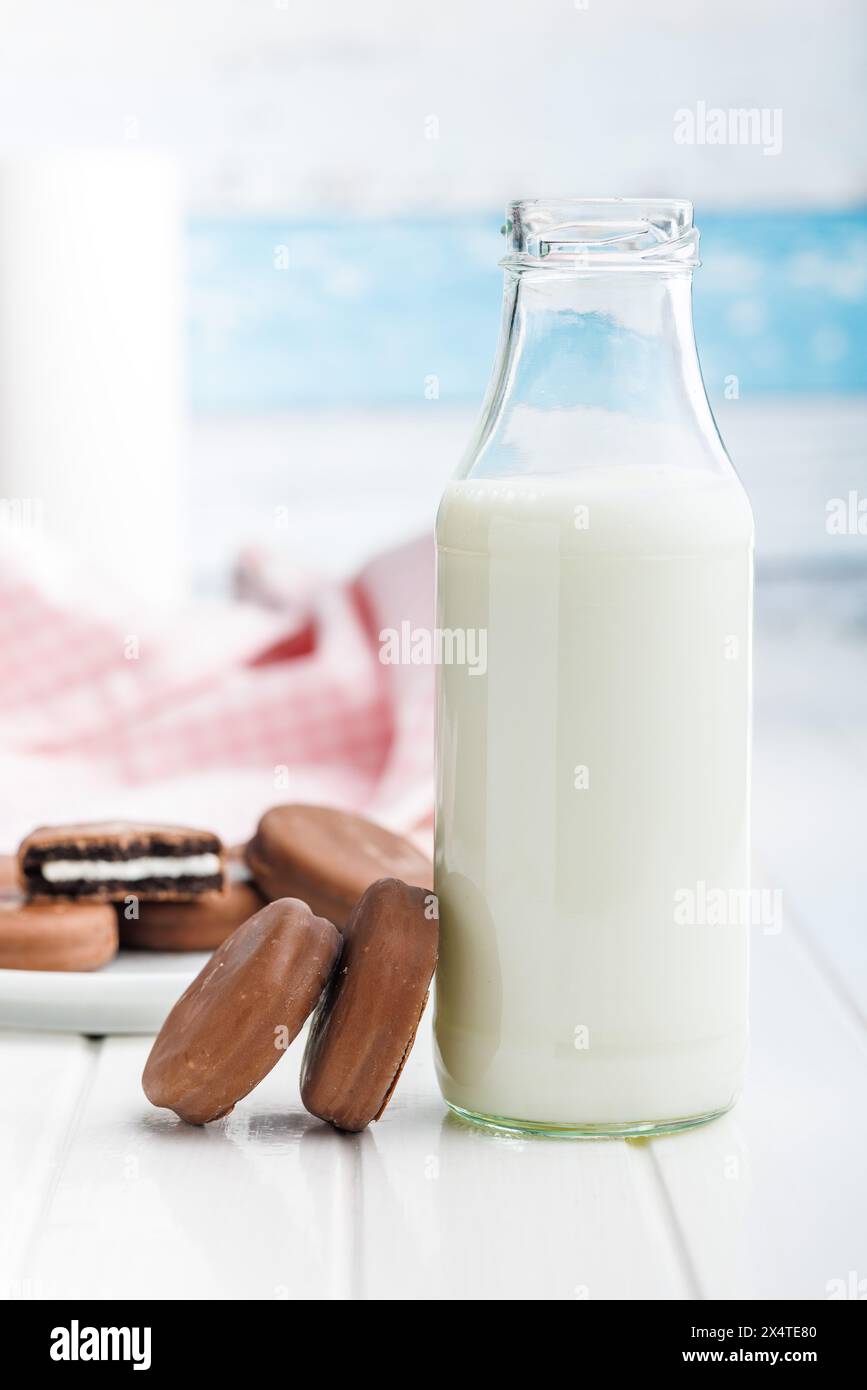 Biscuits recouverts de chocolat et verre de lait sur une table blanche. Banque D'Images