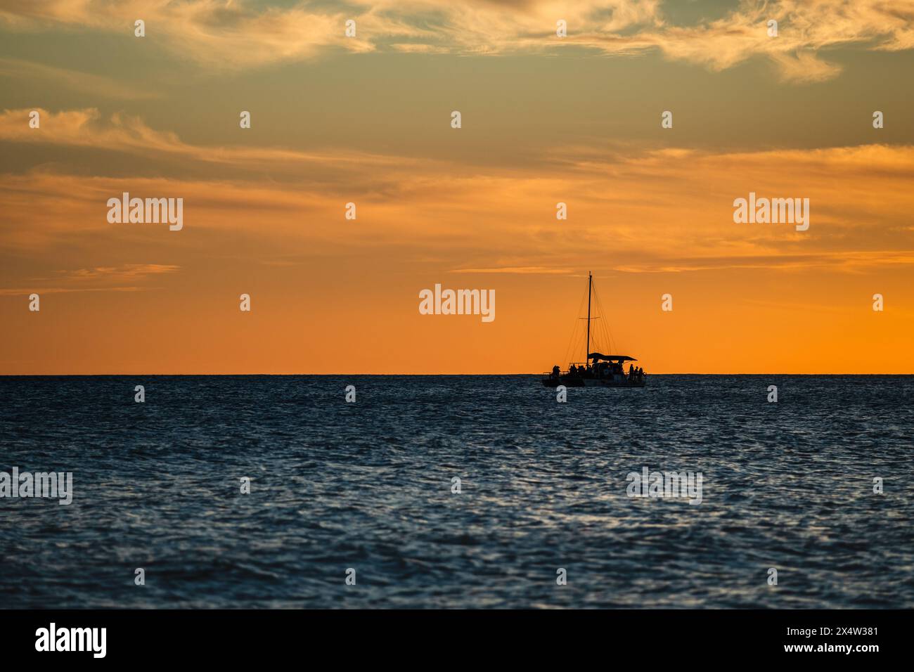 Un bateau navigue dans l'océan au coucher du soleil. Le ciel est orange et l'eau est calme Banque D'Images