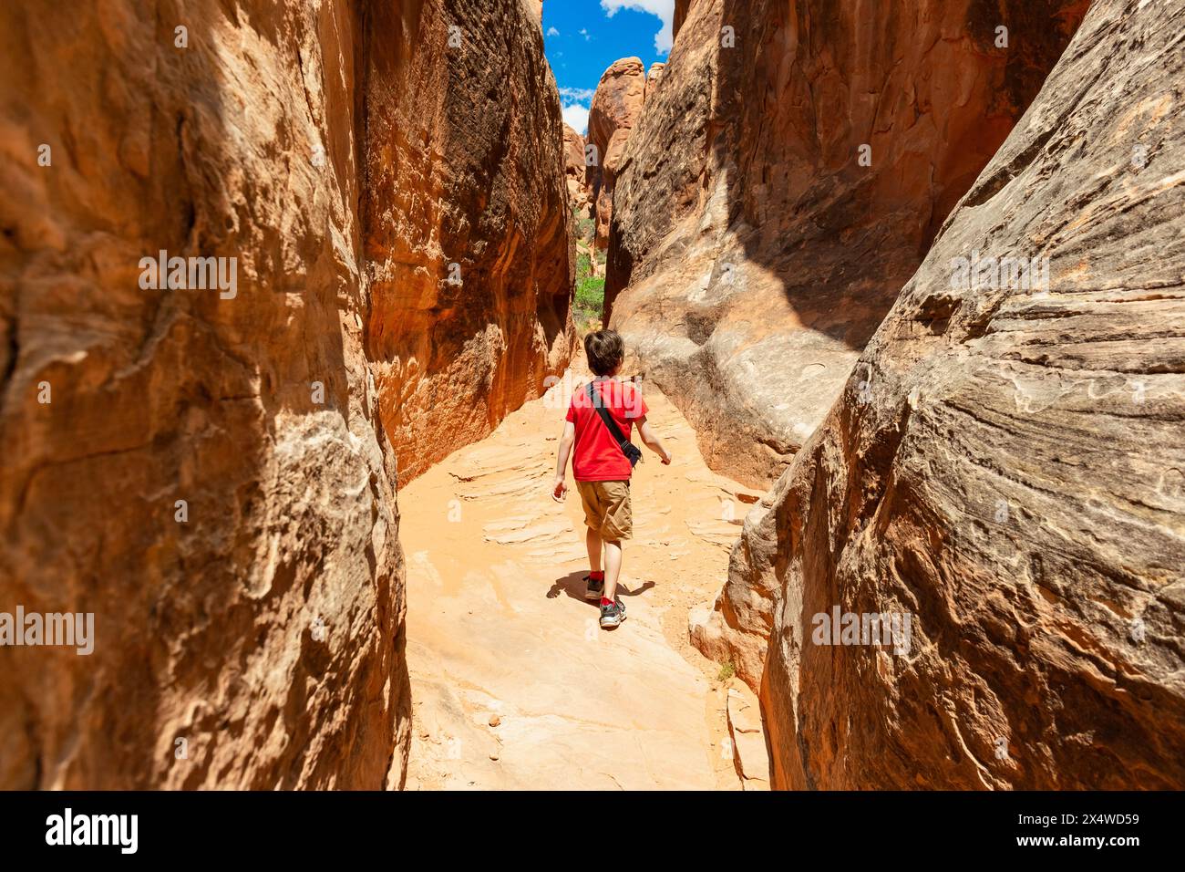 Garçon marchant à l'intérieur du Narrow Sandstone Desert Rock Canyon dans Fiery Furnace Hiking Trail, Arches National Park, Utah, États-Unis Banque D'Images