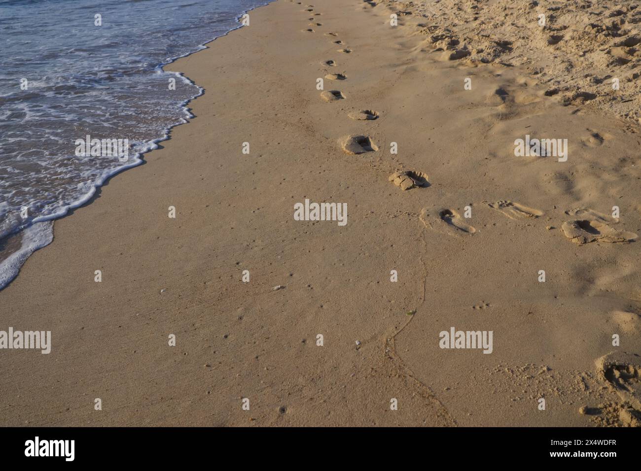 empreintes de pas sur le sable à côté des vagues et de la mer, comme le coucher de soleil tombe un jour d'été Banque D'Images