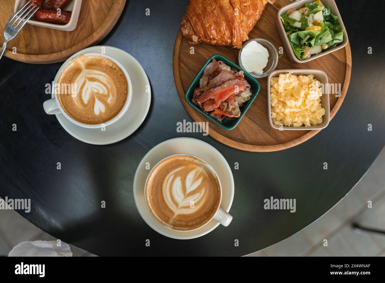 Vue aérienne de deux petits déjeuners avec oeuf brouillé, saucisse, bacon, salade, croissant, café et eau sur une table Banque D'Images