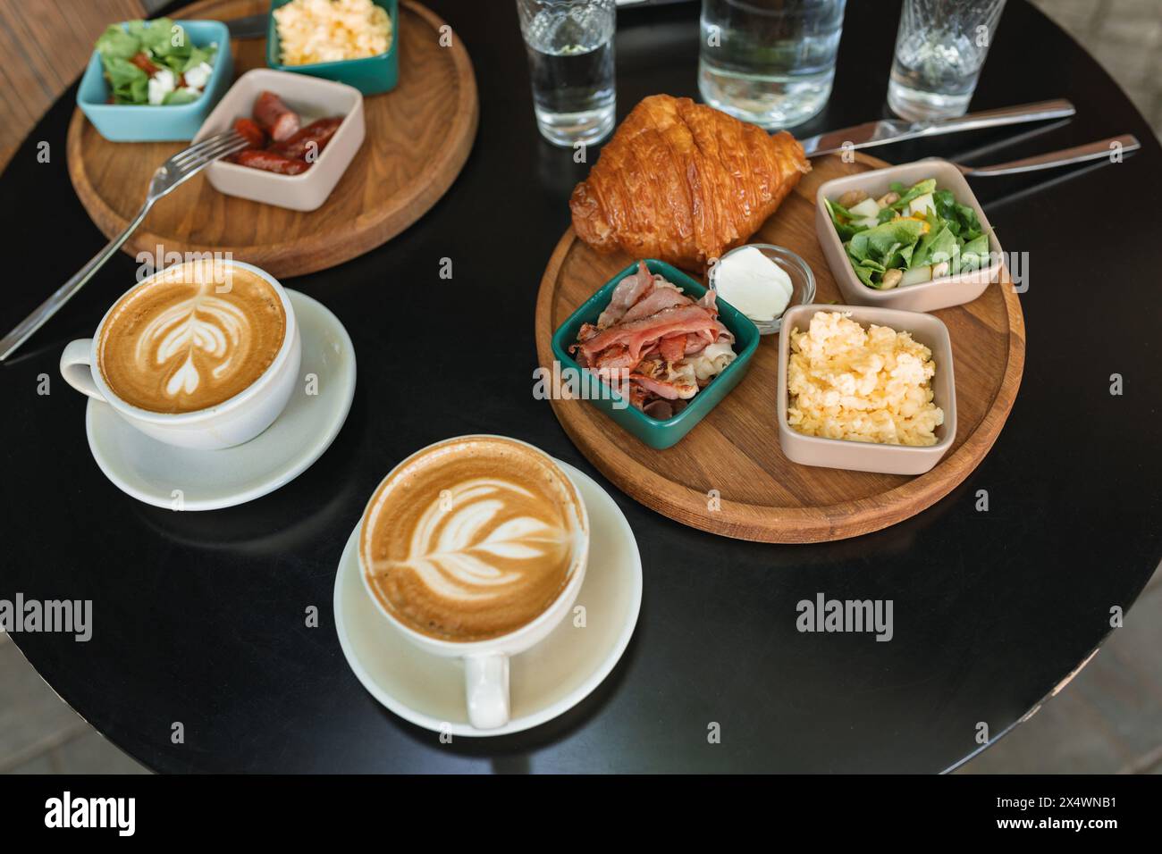 Gros plan de deux petits déjeuners avec oeuf brouillé, saucisse, bacon, salade, croissant, café et eau sur une table Banque D'Images