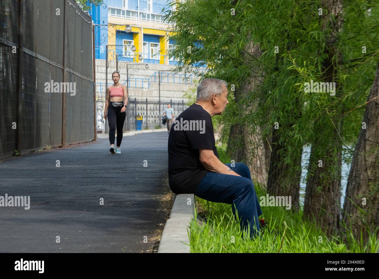 Un homme est assis sur un trottoir au bord de la rivière, une femme fait du jogging au bord de l'eau Banque D'Images