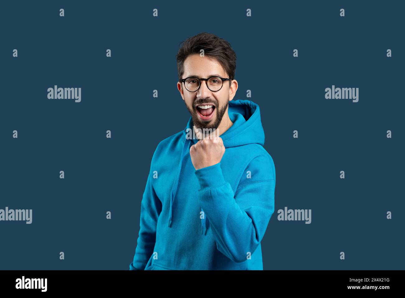 Enthousiaste jeune homme dans Blue Hoodie Cheering sur fond de plaine Banque D'Images