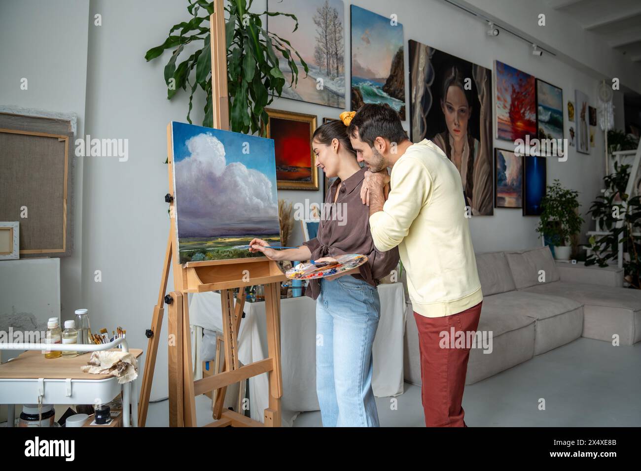 Artiste de femme créative peint l'image dans le studio d'art, mari d'homme aimant de soutien et apprécie le processus Banque D'Images