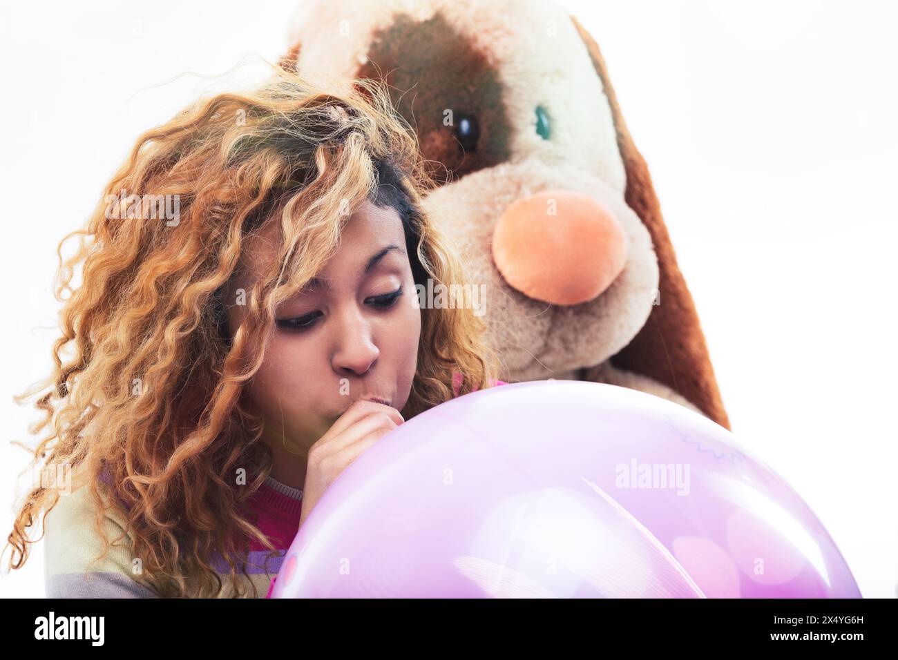 La jeune femme gonfle un grand ballon rose, avec un jouet pour chien en peluche regardant par-dessus son épaule, exprimant une humeur ludique Banque D'Images