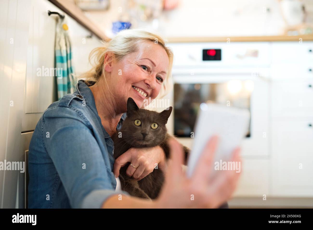 Belle femme mature à la maison, caressant son chat. Femme plus âgée vivant seule, profitant de la journée paisible du week-end Banque D'Images