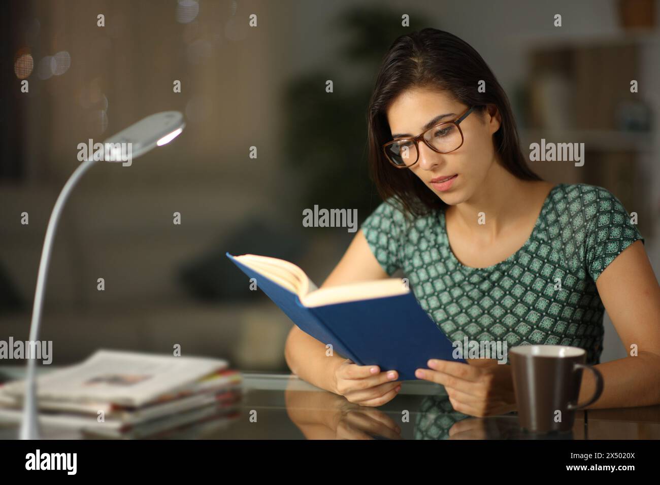 Femme heureuse portant des lunettes lisant un livre de papier dans la nuit à la maison Banque D'Images